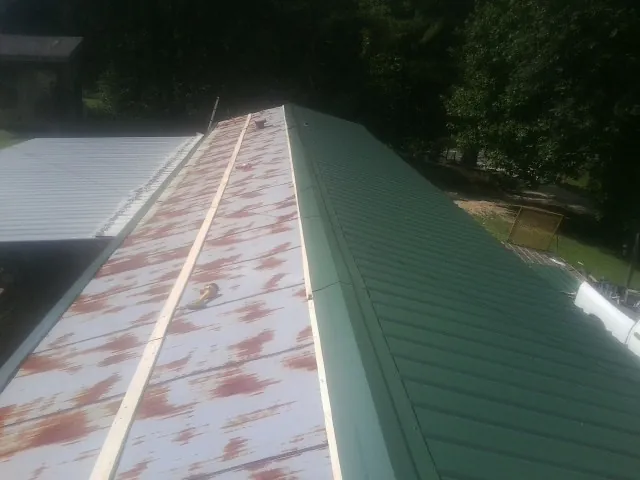 Old rusted panels beside newly installed green metal roofing — Wind Damage Roof Repair by Roofing Brothers in Torrington