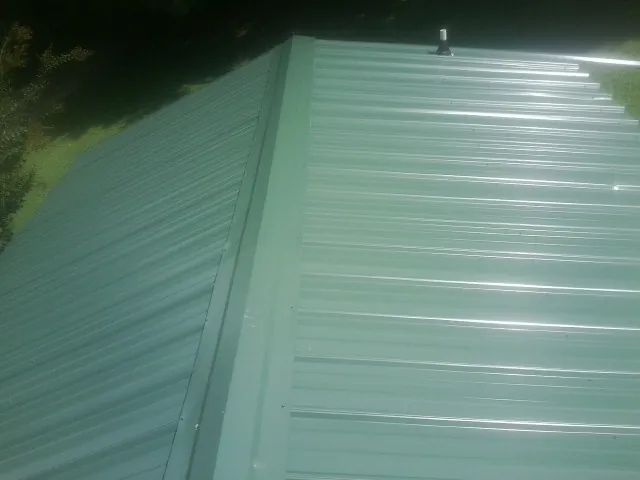 New green metal panels meeting at the ridge of a roof — Flat Roof Repair work by our crew in Torrington
