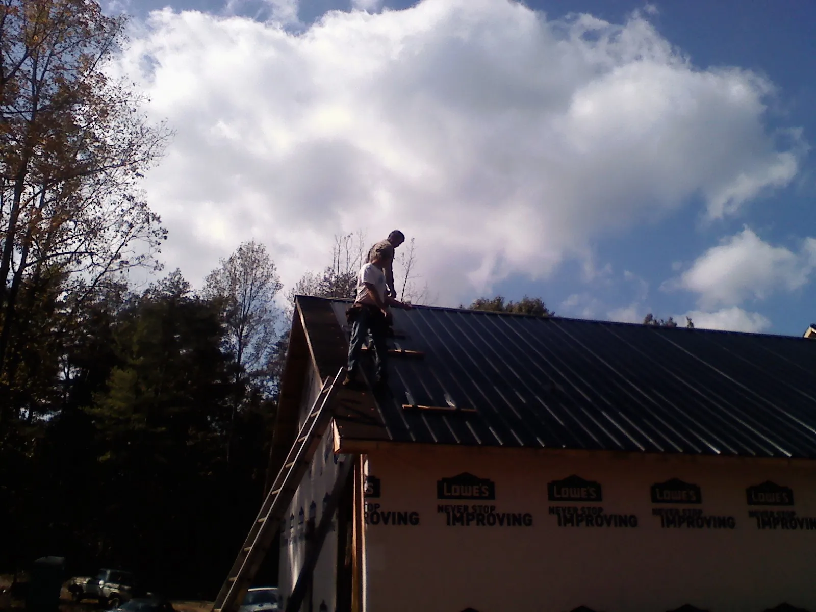 Roofer fastening dark metal panels high against a cloudy sky, from a Roof Inspection job in Torrington