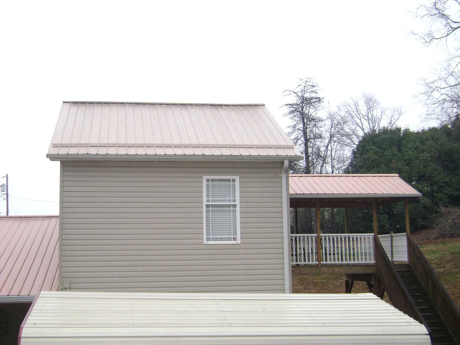 Tan metal roofs on a two story addition and attached porch, from a Roof Replacement job in Torrington